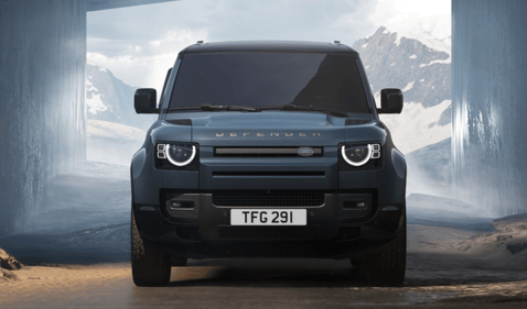 Front view of a blue Defender with circular LED headlights in a mountainous landscape.
