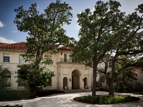 Tree-lined view of a grand mansion entrance with arched doorway.