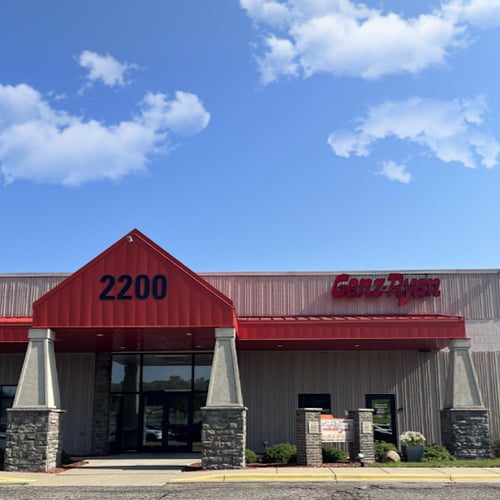 Front entrance of Genz-Ryan Heating, Cooling, Plumbing & Electrical at 2200 in Burnsville, MN, showing the red awning, stone pillars, and company logo under a bright blue sky.