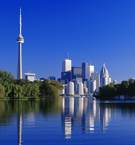 A sunny view of Toronto's skyline with the CN Tower, reflecting in the calm waters of a lake, framed by lush greenery.