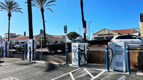 Several EVgo fast charging units installed in marked parking spaces at a public charging station, with EVgo logos on the chargers, protective bollards around each unit