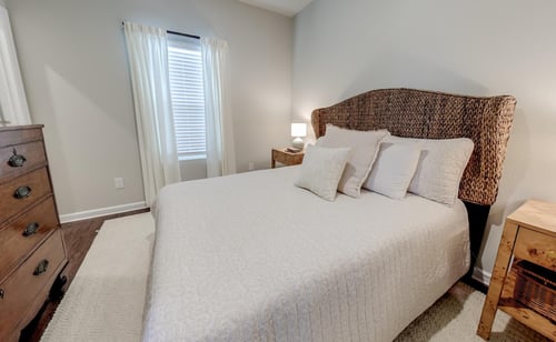 The comfortable apartment home bedroom at Outpost Orchard in Foley, AL, showcases a natural woven headboard, rustic wooden dresser, and soft neutral bedding.
