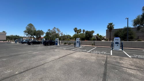 Several EVgo fast charging units installed in marked parking spaces at a public charging station, with EVgo logos on the chargers, protective bollards around each unit