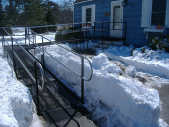 A black steel wheelchair ramp in front of a house providing access after a winter snow storm.