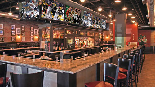Large Bar area at SKYBOKX 109 Sports Bar & Grill in Natick, Massachusetts with Large TVS surrounding the bar to catch all the action. Booth seating in the background.