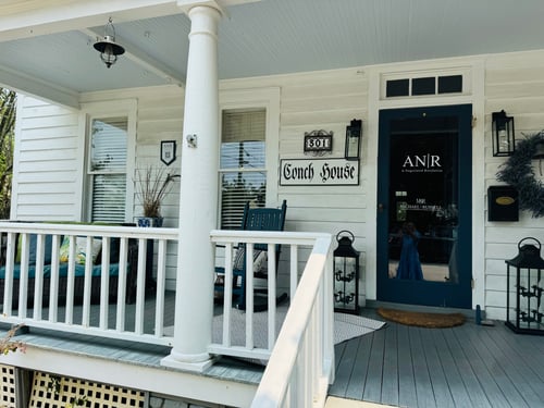 White house with white pillers and blue door with chairs and lanterns