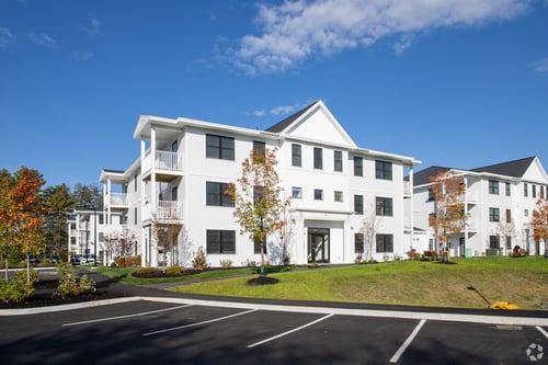 A large white building with a black roof and a parking lot in front.