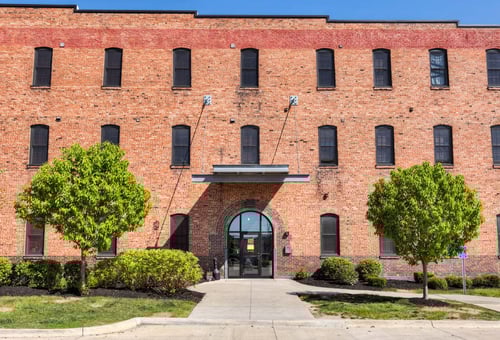 A red brick building with a large arched entrance and two trees in front.at Riverpoint Lofts, Des Moines, IA