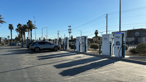 Several EVgo fast-charging units installed in marked parking spaces at a public charging station, with EVgo logos on the chargers, protective bollards around each unit