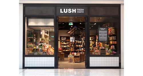 Shopfront, doorway in centre with large glass windows either side. Black frame. Logo above doorway, white font on black background.
