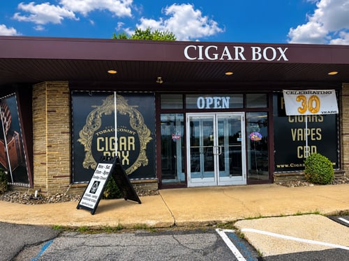 Front exterior of Cigar Box, a premium cigar shop featuring a clean storefront, prominent business signage, welcoming entrance, illuminated OPEN sign, and specialty tobacco retail displays. This image highlights the business location and customer-friendly storefront for local business listings.