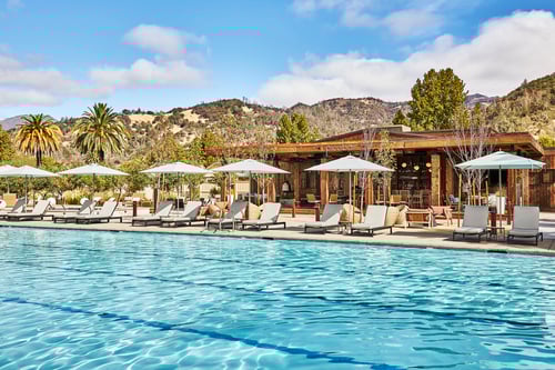 A large outdoor pool with lounge chairs and umbrellas surrounded by hills.
