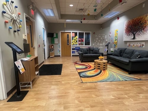 Bright and welcoming lobby with chairs for parents and a colorful bulletin board displaying cute moments from the daycare.