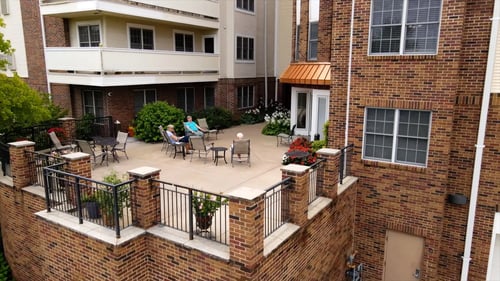 Residents sitting out on the raised brick patio at Bethesda Gardens, with balconies and a copper awning above