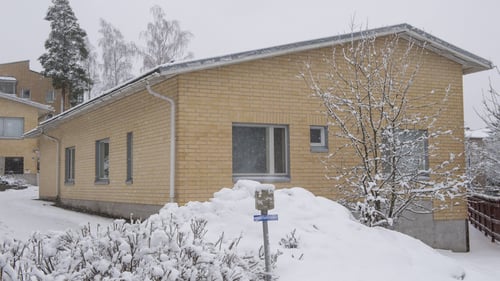 Kuvassa on kellanvaalea yksikerroksinen tiilirakennus lumisessa maisemassa.