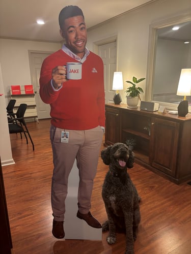 A dog sitting next to a card board cut out of Jake from State Farm.