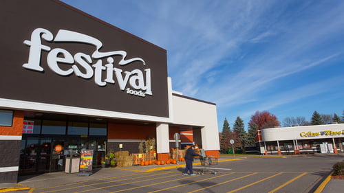 Person wearing all black pushing a shopping cart away from pumpkin lined entrance of Festival Foods at White Bear Hills Shopping Center