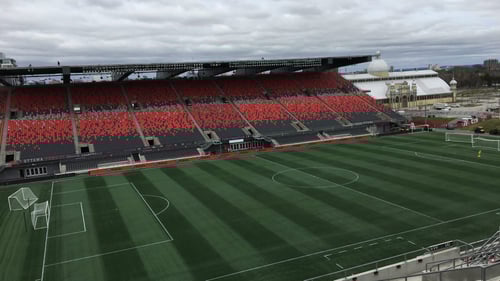Empty soccer stadium with vivid red and black seats and verdant green field under an overcast sky. The atmosphere is calm and serene, reflecting a quiet moment.