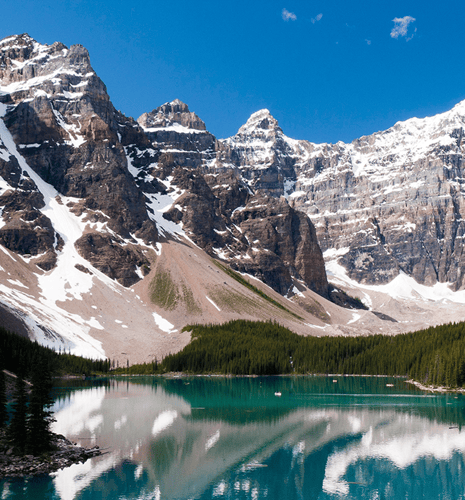 Snow-capped mountains tower over a tranquil turquoise lake, reflecting the peaks and surrounding evergreen forest under a clear blue sky. Serene and majestic.