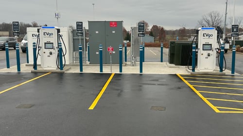 Several EVgo fast-charging units installed in marked parking spaces at a public charging station, with EVgo logos on the chargers, protective bollards around each unit