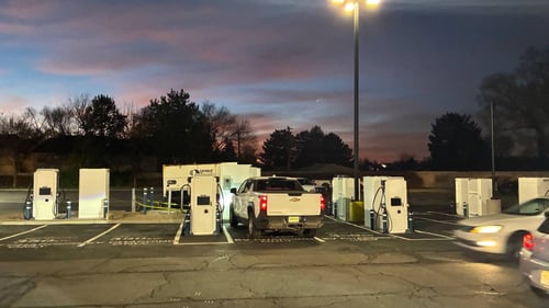 Several EVgo fast-charging units installed in marked parking spaces at a public charging station, with EVgo logos on the chargers, protective bollards around each unit