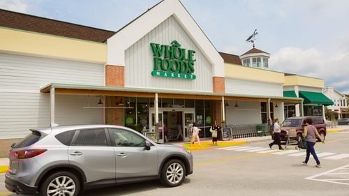 Silver hatchback passing people at entrance of Whole Foods at The Shoppes at Fox Run shopping center