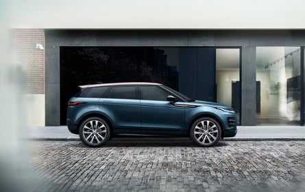 Side view of a blue Range Rover Velar parked on a cobblestone street in front of a modern building.