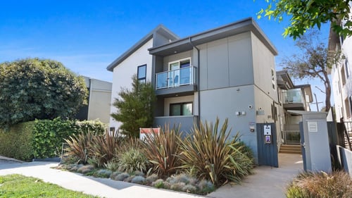 an apartment building with a sidewalk and plants in front of it