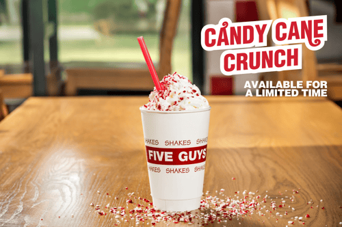 An image of a Five Guys milkshake featuring the limited-time Candy Cane Crunch mix-in sitting on a table in a Five Guys restaurant.