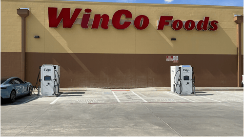 Several EVgo fast-charging units installed in marked parking spaces at a public charging station, with EVgo logos on the chargers, protective bollards around each unit