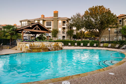 A swimming pool in front of a building with a tree to the right.