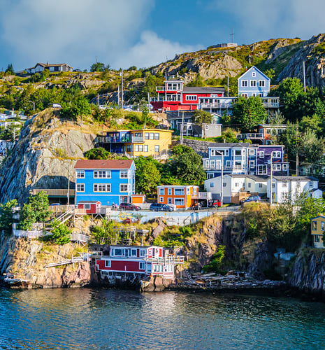 Colorful hillside houses in St. John's, Newfoundland, overlook the water. Vibrant blue, red, yellow, and purple homes create a lively, picturesque scene.