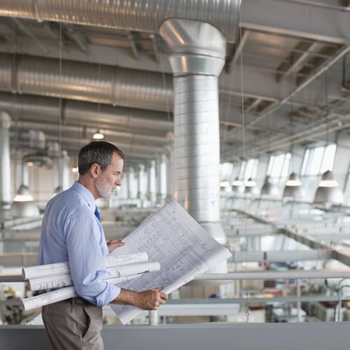 Architect reviewing blueprints in a modern industrial facility showcasing precision and professional expertise.