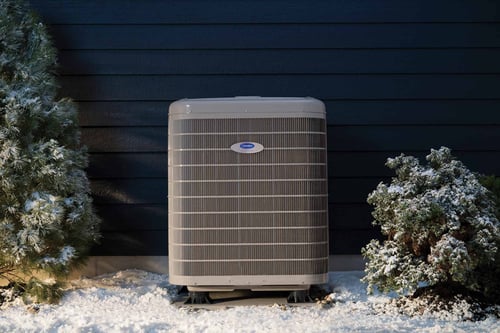 An Infinity heat pump installed outside a home in winter snow