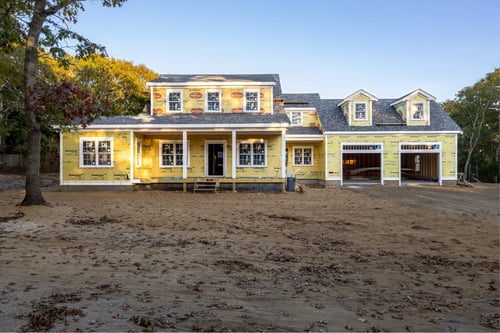 A bright yellow house featuring a garage, prominently located in the midst of an expansive field.