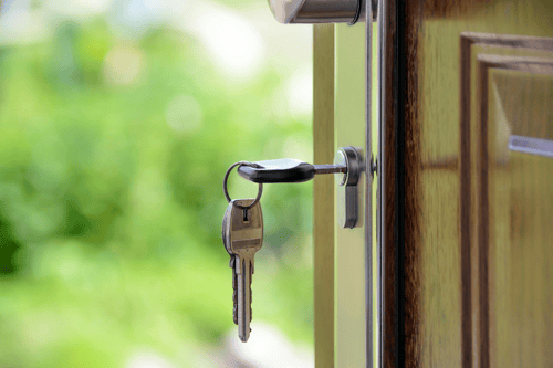 Close-up shot of a set of keys in the lock of an open door that leads out to a green lawn.