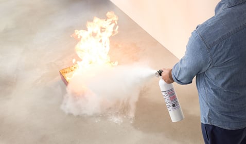 Person putting out a fire using a Kidde Fire Extinguisher.