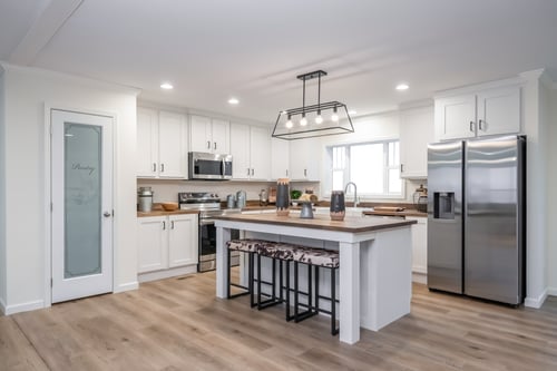 Modern kitchen in a manufactured home with island, white cabinets, and stainless-steel appliances.