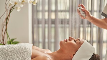 A spa therapist gives a relaxing treatment to a client lying on a treatment bed, surrounded by a serene setting with soft lighting and a white orchid flower in the background.