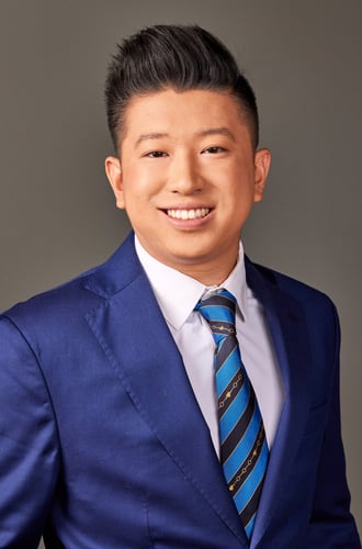Team member Derrick standing and smiling wearing navy blue suit