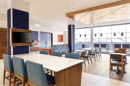 Bright modern hotel lobby with blue chairs and a TV screen.