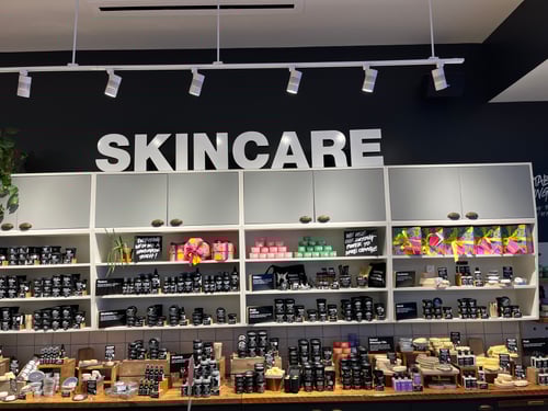 Large wall shelf unit and wooden floor display unit housing packaged and unpackaged skincare products. Sign above reads Skincare