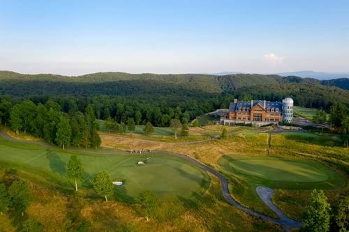 Blue mountains under clear sky with trees and a golf course.