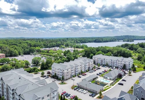 Aerial view of apartment complex with pool, parking, and lake in background.