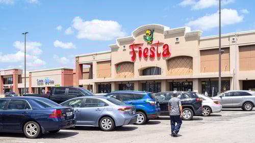 Man in t-shirt walking through full parking lot towards Fiesta grocery store at Westheimer Commons shopping center