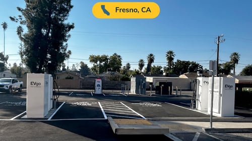 Several EVgo fast-charging units installed in marked parking spaces at a public charging station, with EVgo logos on the chargers, protective bollards around each unit
