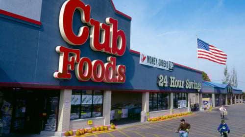 Kids riding their bikes in front of pumpkin lined entrance of Cub Foods