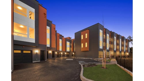 A modern building with orange and grey exterior is illuminated from within at The Narrows at Clare Apartments , Bremerton, WA, 98310