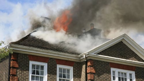 Smoke and flames billowing from the roof of a brick house.