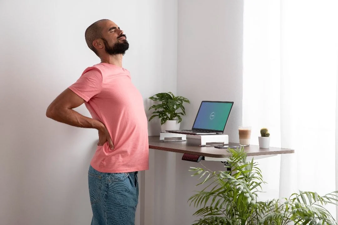man at standing desk holding his back in pain